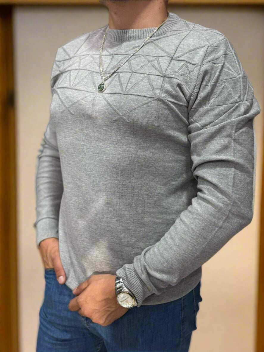 Person wearing a gray sweater with a geometric pattern, standing against a neutral background.
